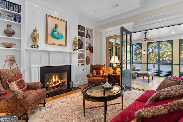 living room featuring ceiling fan, light hardwood / wood-style flooring, ornamental molding, and built in shelves