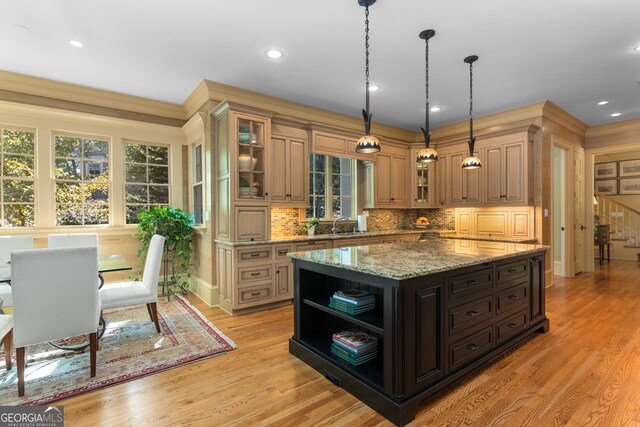 kitchen featuring light stone counters, hanging light fixtures, backsplash, a center island, and light wood-type flooring