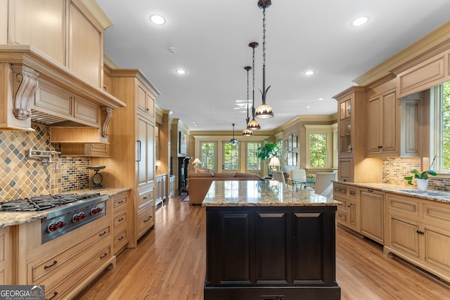 kitchen with hanging light fixtures, a kitchen island, light stone countertops, light wood-type flooring, and stainless steel gas stovetop