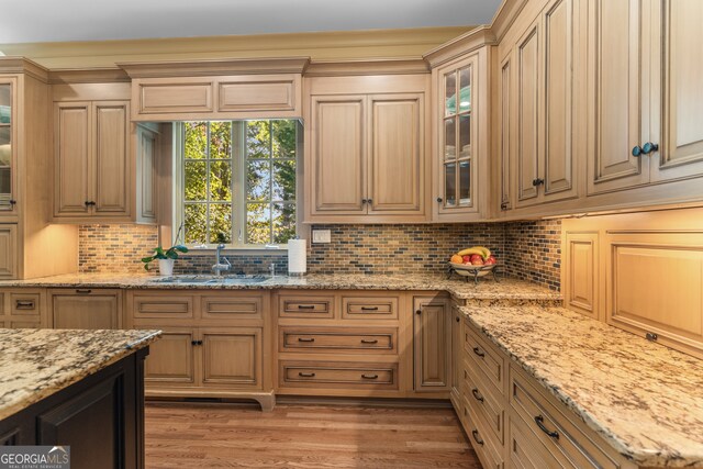 kitchen featuring backsplash, light stone countertops, hardwood / wood-style floors, and sink