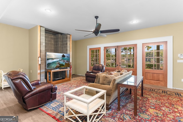 living room featuring ceiling fan, french doors, hardwood / wood-style floors, and a large fireplace