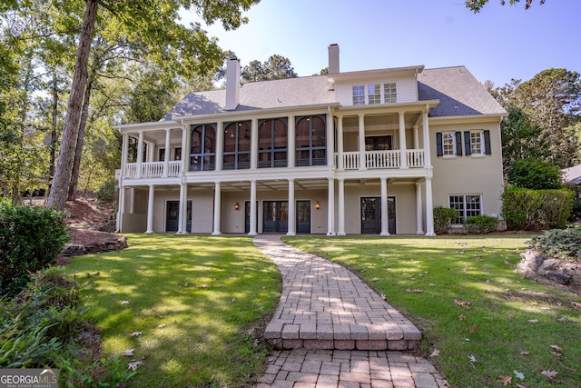 rear view of house featuring a balcony and a lawn