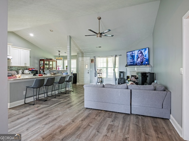 living room with light hardwood / wood-style flooring, vaulted ceiling, ceiling fan, and a textured ceiling