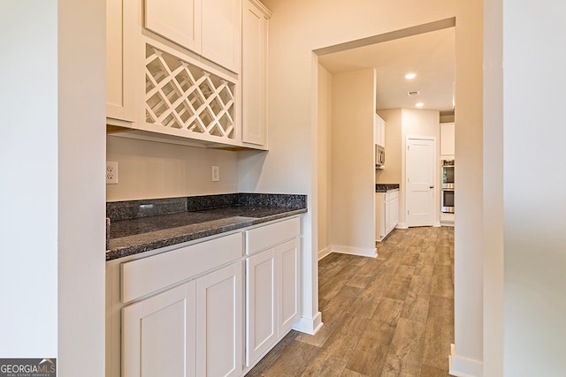 bar featuring light hardwood / wood-style floors, dark stone countertops, and white cabinets