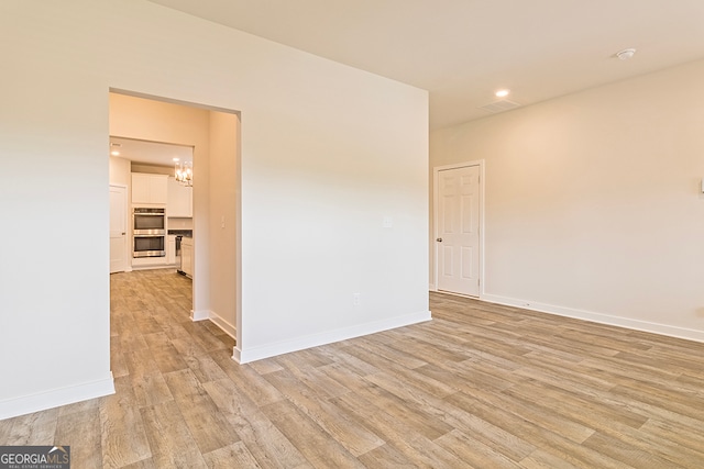 unfurnished room featuring light wood-type flooring and an inviting chandelier