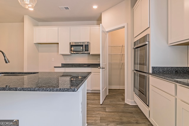 kitchen featuring appliances with stainless steel finishes, dark stone counters, and white cabinets