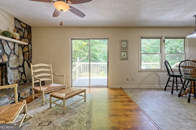 living room with ceiling fan, a textured ceiling, a fireplace, and wood-type flooring