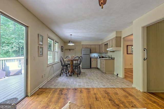 kitchen featuring pendant lighting, stainless steel refrigerator, sink, and light hardwood / wood-style floors