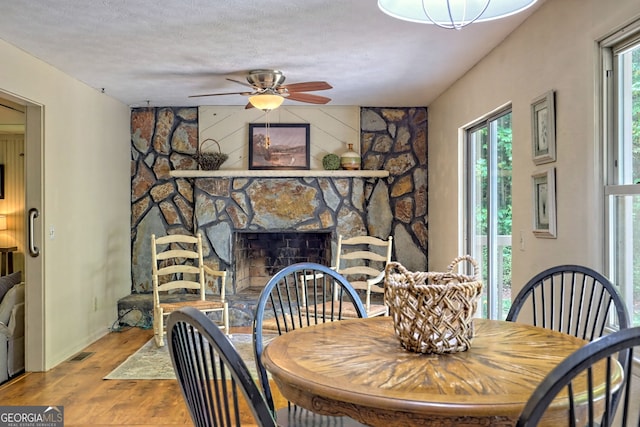 dining space with a fireplace, ceiling fan, hardwood / wood-style flooring, and a textured ceiling