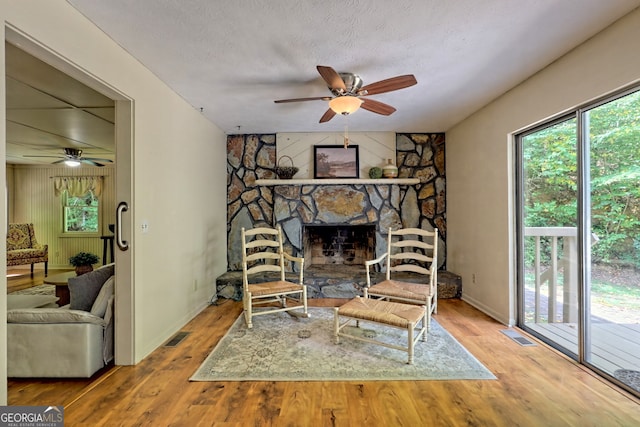 sitting room with hardwood / wood-style flooring, a stone fireplace, and a textured ceiling