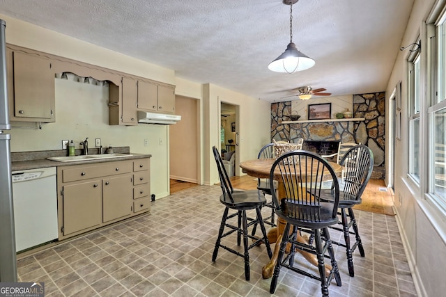 kitchen featuring sink, white dishwasher, a fireplace, hanging light fixtures, and a textured ceiling