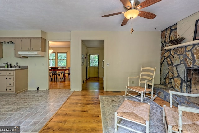 living room with ceiling fan, a textured ceiling, light hardwood / wood-style flooring, and sink