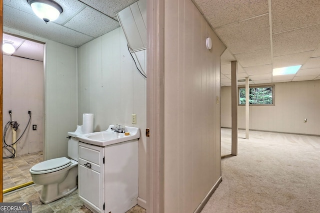 bathroom featuring walk in shower, toilet, a paneled ceiling, wooden walls, and vanity