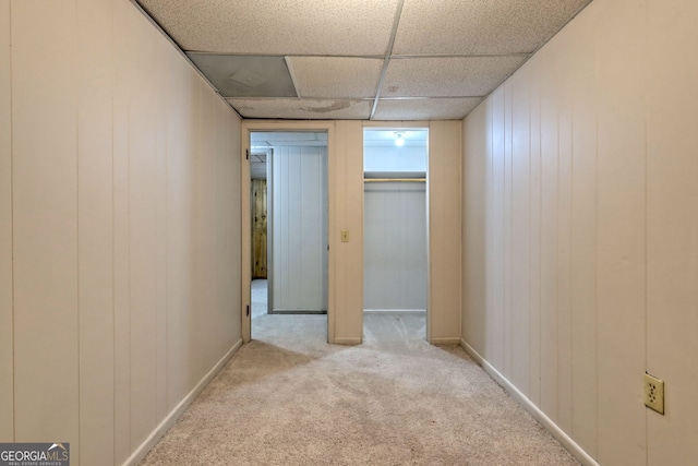 interior space with a paneled ceiling, wood walls, and light carpet