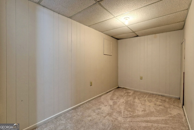 basement with light carpet, a paneled ceiling, and wood walls