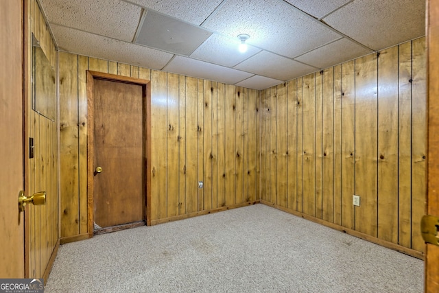 basement featuring light carpet, wooden walls, and a paneled ceiling