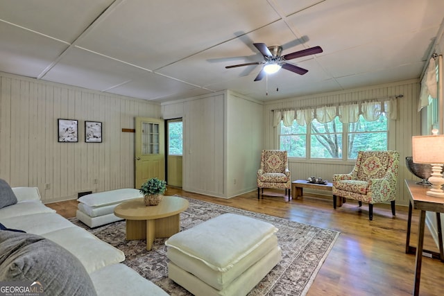 living room with wood-type flooring, wooden walls, and ceiling fan