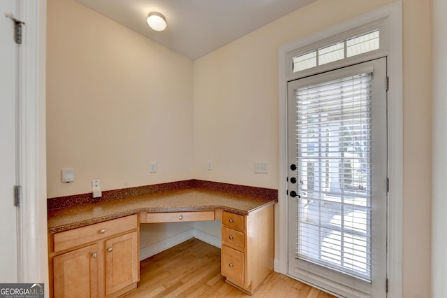 unfurnished office featuring built in desk and light hardwood / wood-style floors