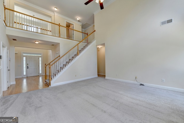 unfurnished living room with light carpet, a towering ceiling, and ceiling fan