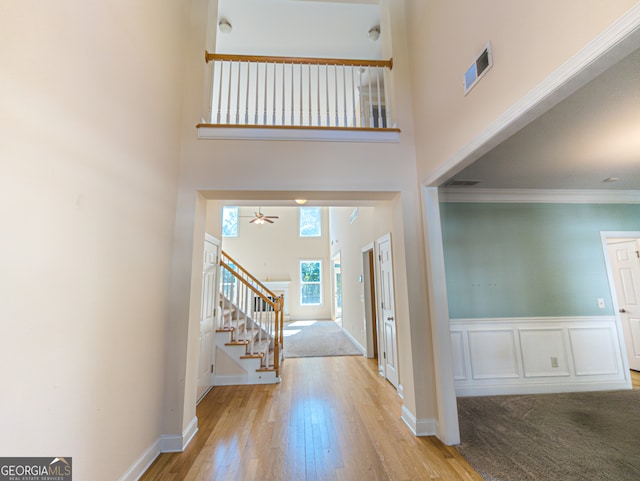 foyer featuring light wood-type flooring, a towering ceiling, and crown molding