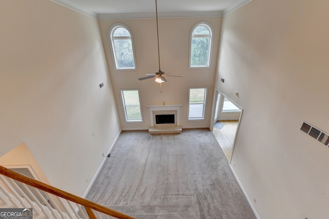 unfurnished living room with ceiling fan, crown molding, a high ceiling, and a wealth of natural light