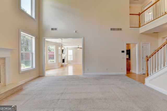 unfurnished living room with ceiling fan, a high end fireplace, a high ceiling, light colored carpet, and crown molding