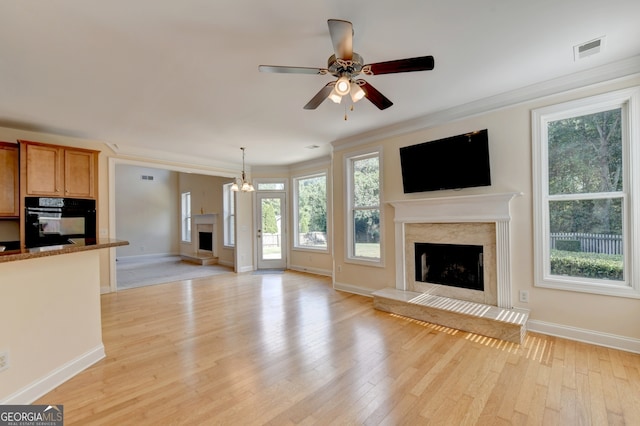 unfurnished living room with ceiling fan with notable chandelier, light wood-type flooring, a premium fireplace, and crown molding