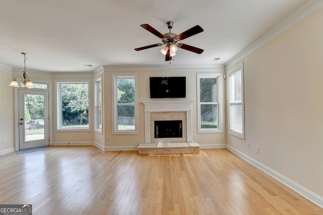 unfurnished living room featuring light wood-type flooring, ceiling fan with notable chandelier, plenty of natural light, and crown molding