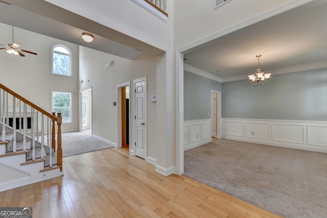 carpeted foyer featuring ceiling fan with notable chandelier, a towering ceiling, and crown molding