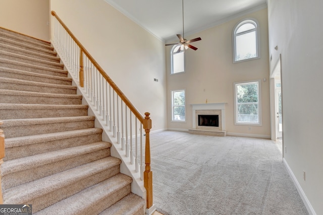 stairs with a high ceiling, ceiling fan, plenty of natural light, and a fireplace