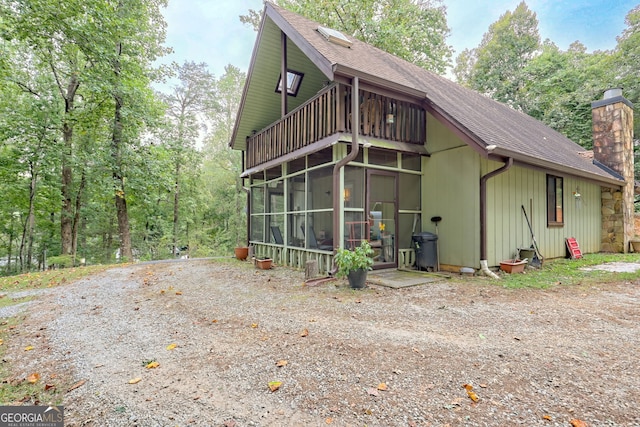 rear view of property featuring a shingled roof, a sunroom, a chimney, and a balcony