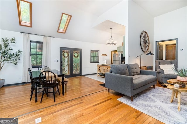 living room featuring high vaulted ceiling, a skylight, light wood-style floors, french doors, and an inviting chandelier