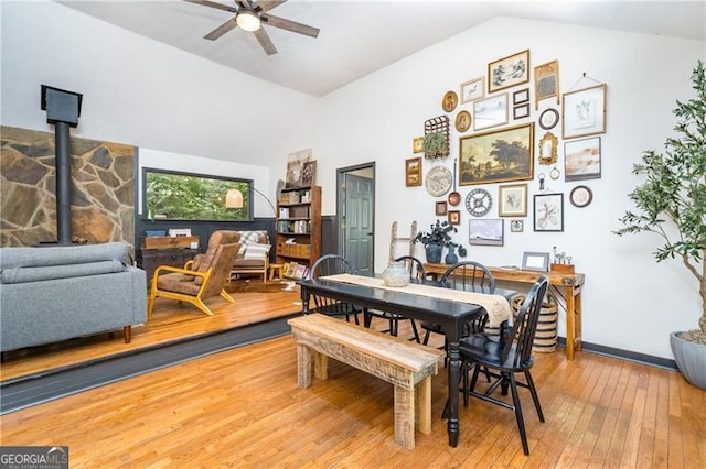 dining space with lofted ceiling, a ceiling fan, a wood stove, wood finished floors, and baseboards