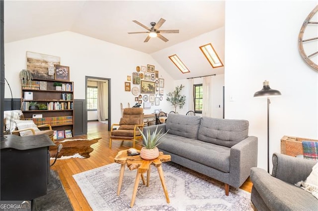 living room featuring lofted ceiling with skylight, a ceiling fan, and wood finished floors