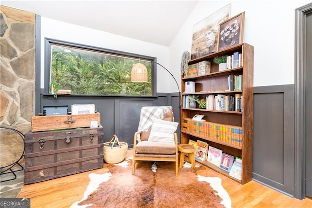 living area featuring light wood-style floors, a decorative wall, vaulted ceiling, and wainscoting