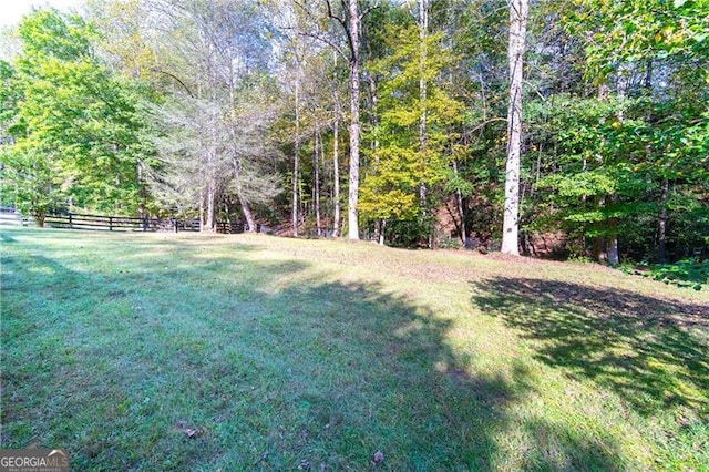 view of yard featuring a wooded view and fence