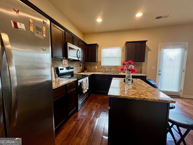 kitchen with tasteful backsplash, a kitchen island, stainless steel appliances, light stone countertops, and dark hardwood / wood-style flooring