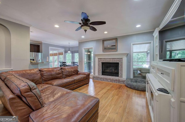 living room with light hardwood / wood-style flooring, a brick fireplace, ceiling fan, and ornamental molding