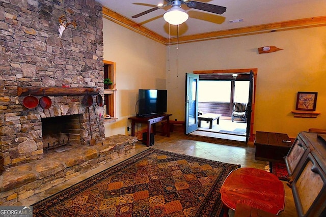 living room featuring ceiling fan, a stone fireplace, crown molding, and light tile patterned floors