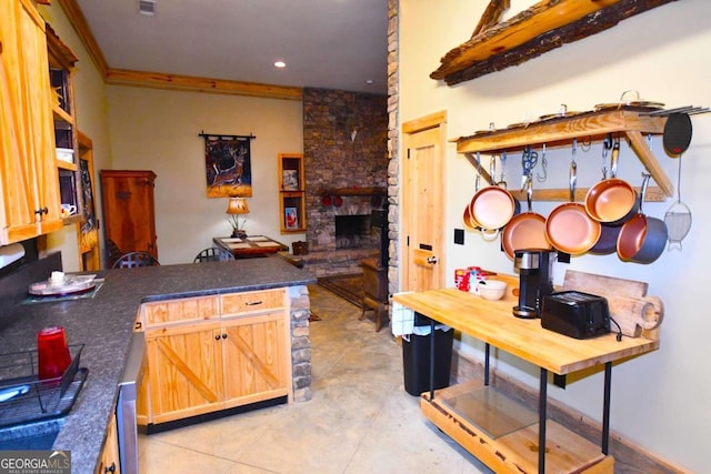 kitchen with ornamental molding, kitchen peninsula, light tile patterned floors, and a stone fireplace