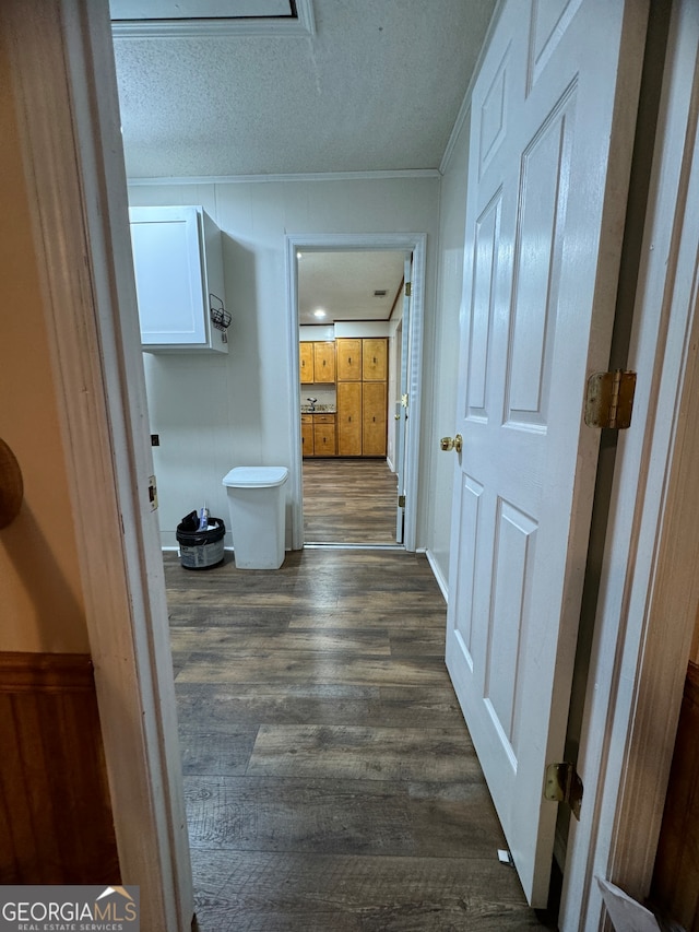 hallway with a textured ceiling, crown molding, and dark wood-type flooring