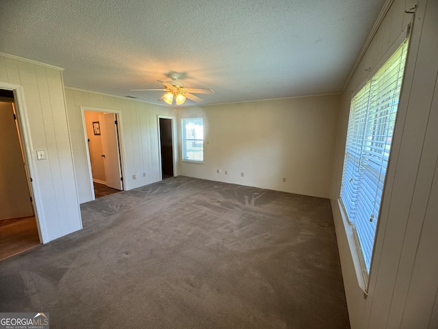 unfurnished bedroom with dark carpet, ornamental molding, multiple windows, and ceiling fan