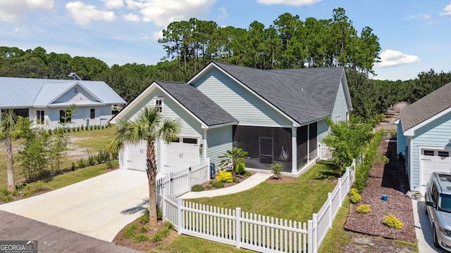 view of front of property with a shingled roof, concrete driveway, a sunroom, a fenced backyard, and a front yard