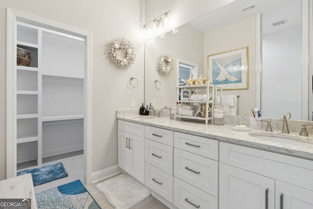 bathroom with double vanity, a sink, visible vents, and a walk in closet