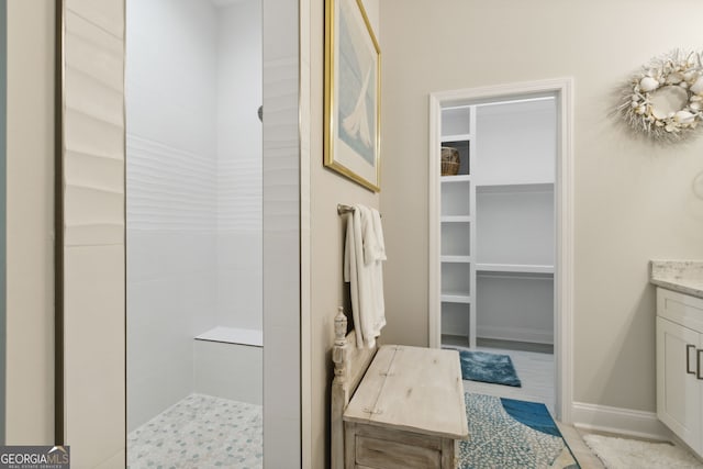 full bath featuring tiled shower, a walk in closet, vanity, and baseboards