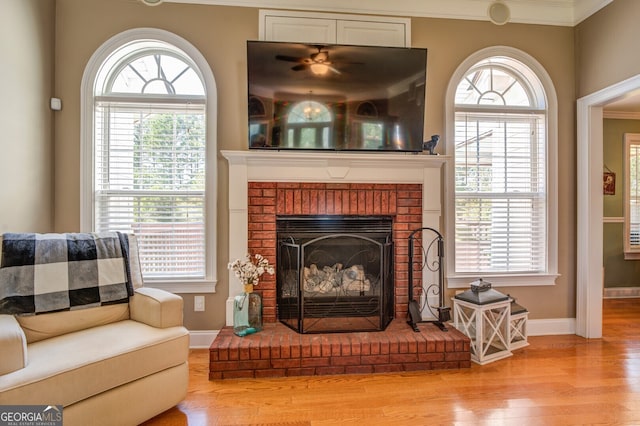 living room with crown molding, light hardwood / wood-style flooring, a brick fireplace, and a wealth of natural light