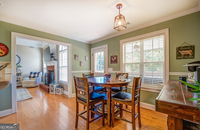 dining area with a fireplace, plenty of natural light, crown molding, and light hardwood / wood-style flooring