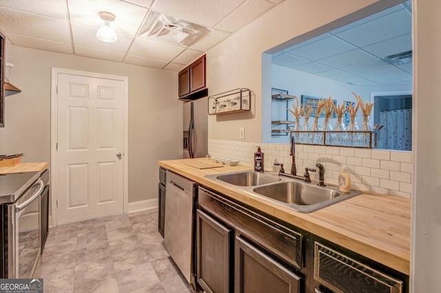 kitchen with sink, decorative backsplash, a drop ceiling, appliances with stainless steel finishes, and butcher block countertops