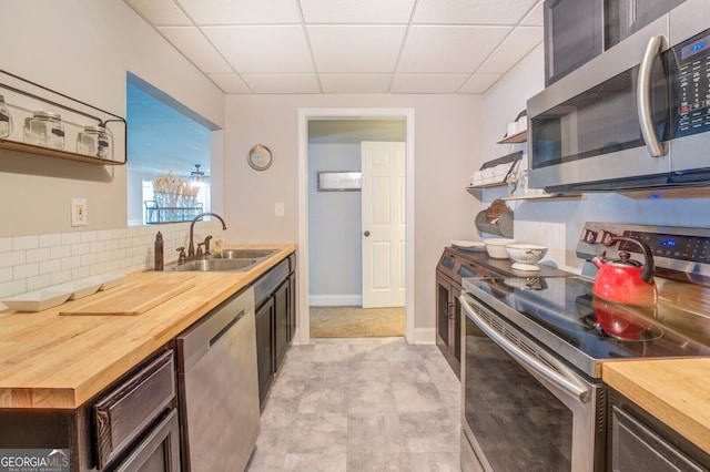 kitchen with appliances with stainless steel finishes, butcher block countertops, a drop ceiling, dark brown cabinets, and sink