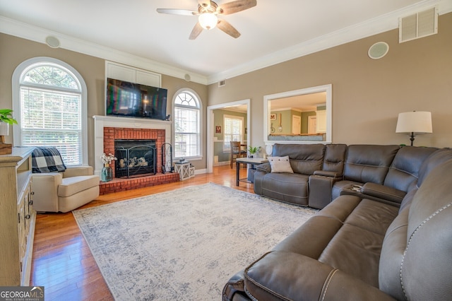 living room with light wood-type flooring, ceiling fan, a brick fireplace, and plenty of natural light